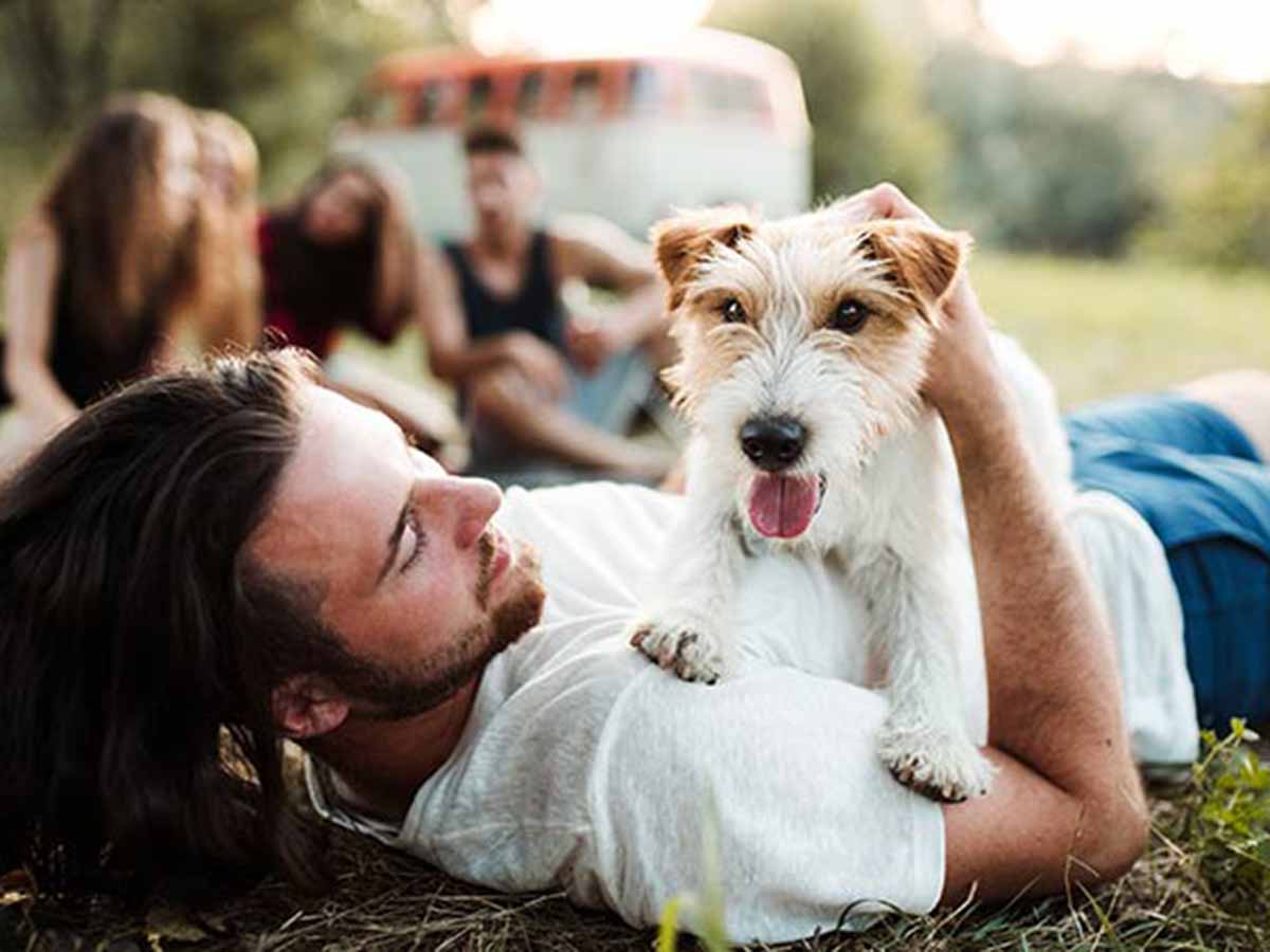 Group of people sitting outside in the grass with a dog laying on a man's chest. 